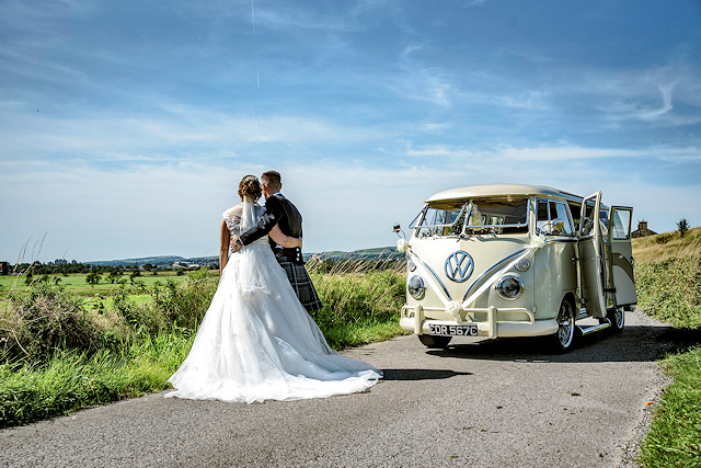 A married couple look over the hills next to a VW van