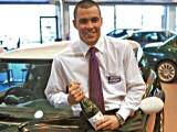 Carcraft sales executive posing with a car and a bottle of champagne