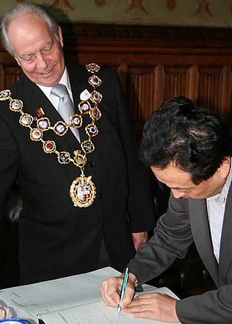 Dr Natori Yuji signs the visitors book at the town hall in front of Mayor Councillor Robin Parker.