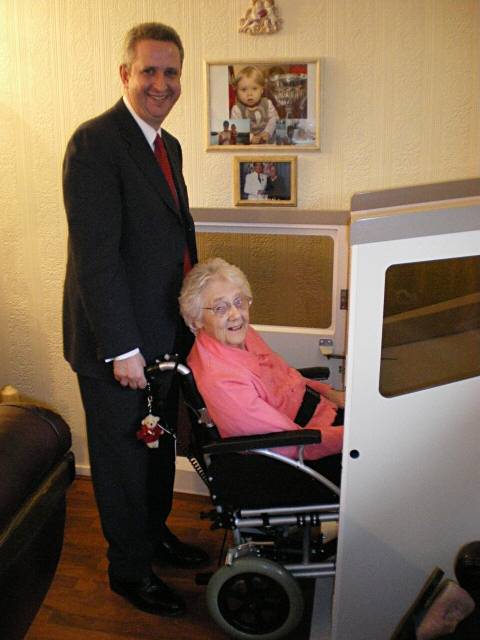 Minister for Care Ivan Lewis helps Janet Riley into the lift installed in her Newhey home