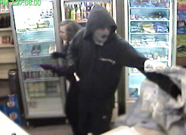 One of the robbers threatens the shopkeeper over the counter.