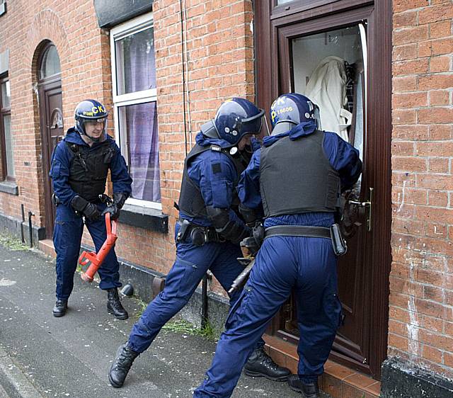 Officers break down a door during this morning's drug raids.