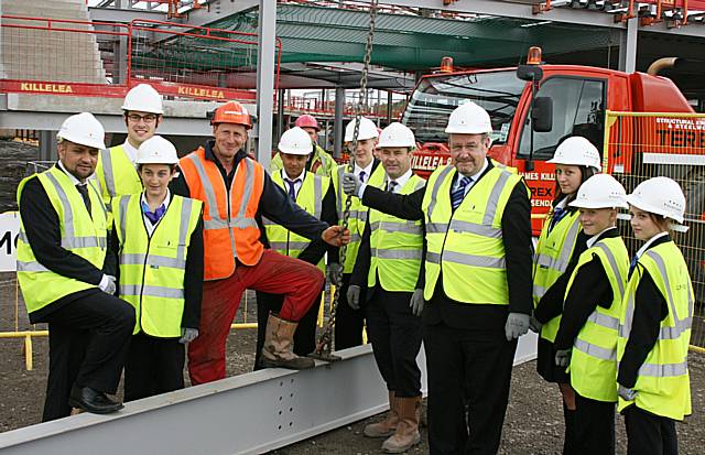 Principal Eric Jackson (fourth from right) alongside pupils and guests celebrate the topping out by helping to raise the final piece of steel.