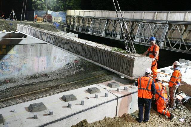 A large crane lowers the first new bridge beam into place across the railway, in the middle of the night