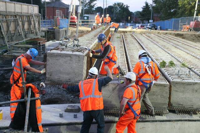 At dawn a large crane lowers concrete bridge beams into place across the railway