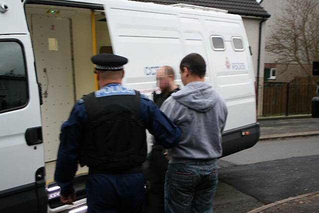 A suspect being led to a police van following early morning raids