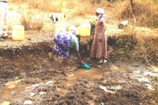 Two women collecting water from the ditch. The women had walked from their home for about 4 hours to find this water which they have to carry back to their homes.