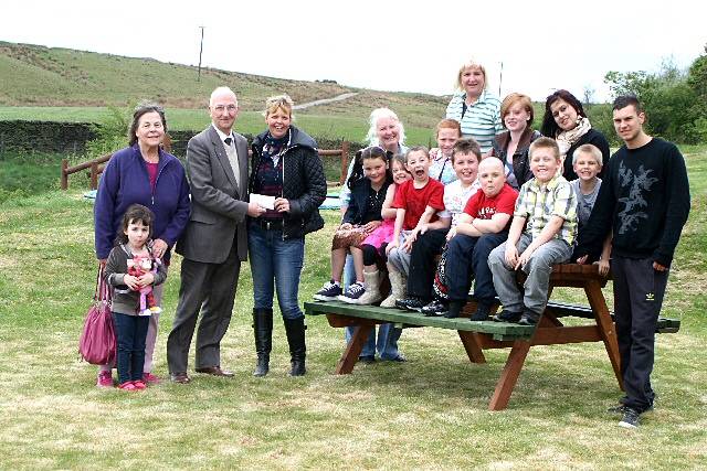 Councillor Evans presenting the cheque to Jane Barker, alongside his wife and granddaughter and children and staff at the home