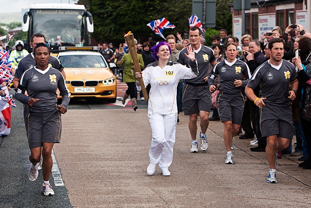 Luci Teal running down Bolton Road with the Olympic Torch in front of hundreds of flag-waving locals 
