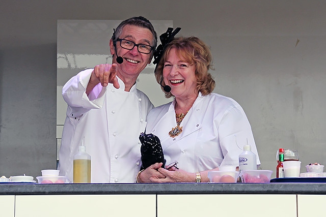 Kevin Woodford cooking in the Feel Good Festival celebrity food kitchen, helped by the Mayoress of Rochdale, Cecile Biant