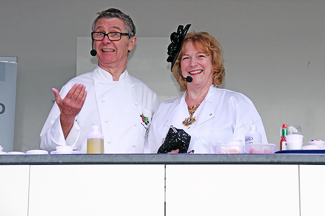 Kevin Woodford cooking in the Feel Good Festival celebrity food kitchen, helped by the Mayoress of Rochdale, Cecile Biant