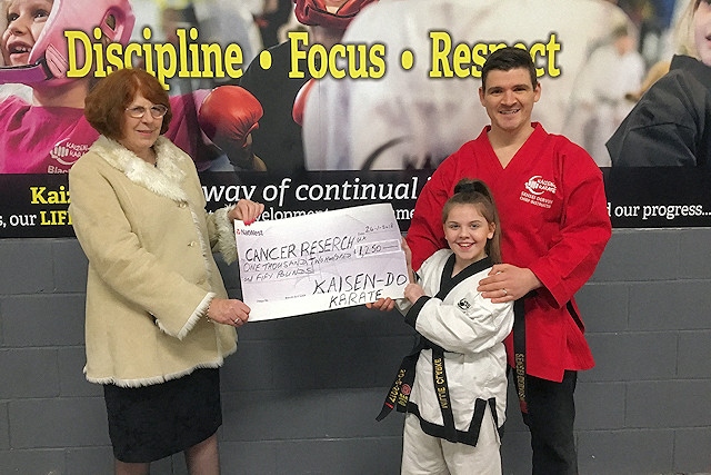 Blackbelt Millie Clarke presents the cheque to Cancer Research