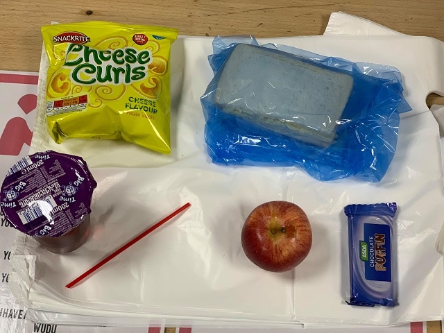 A packed lunch - a sandwich, crisps, apple, chocolate bar and a drink